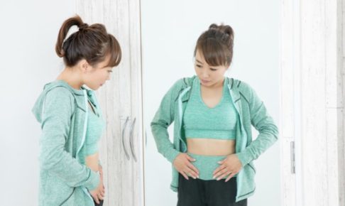 鏡の前で腹のたるみを気にする女性