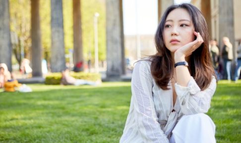 大学の屋外の芝生の上で物思いの深けているアジア人美女