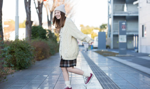 マンションの前で片足立ちしているニットコーデの女性