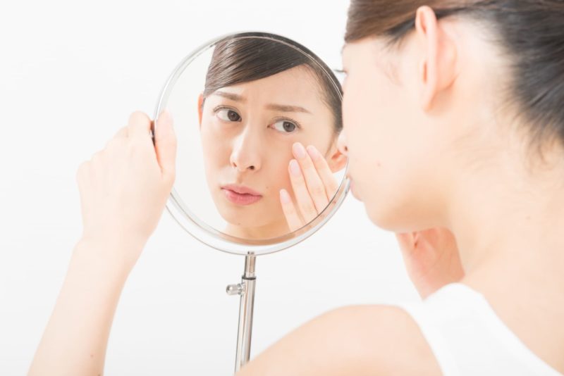 手鏡で目もとのたるみを気にする女性