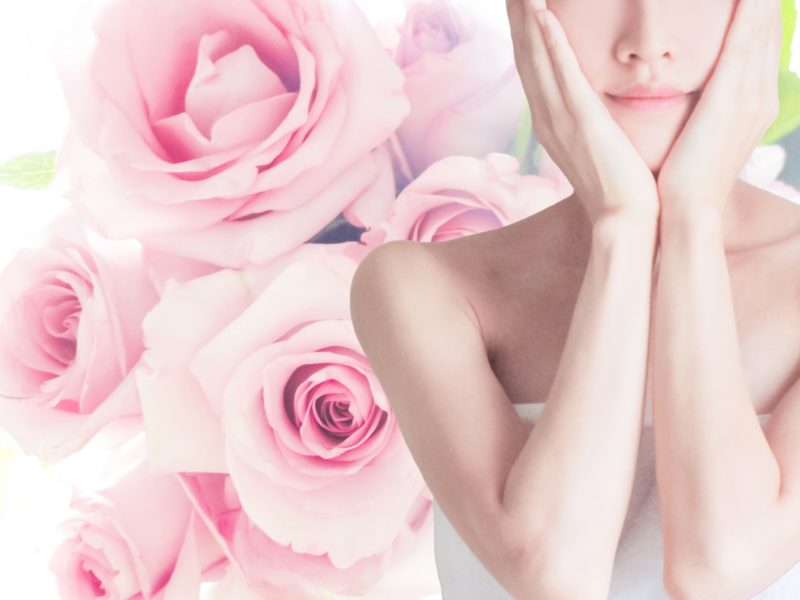 バラを背に自分の顔に触れる女性