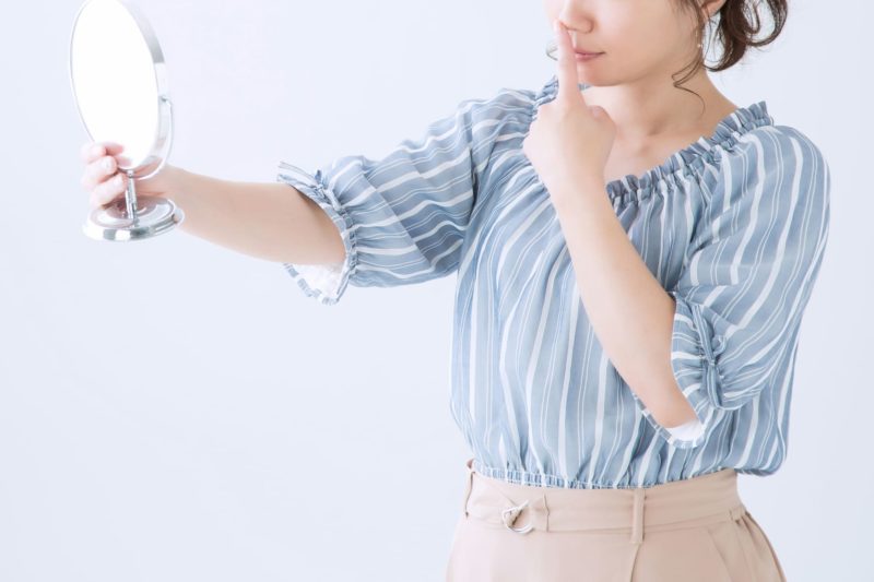 自分の鼻が気になり鏡で見ている青いブラウスの女性