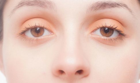 オレンジのアイシャドウをして目を見開いている女性のアップ