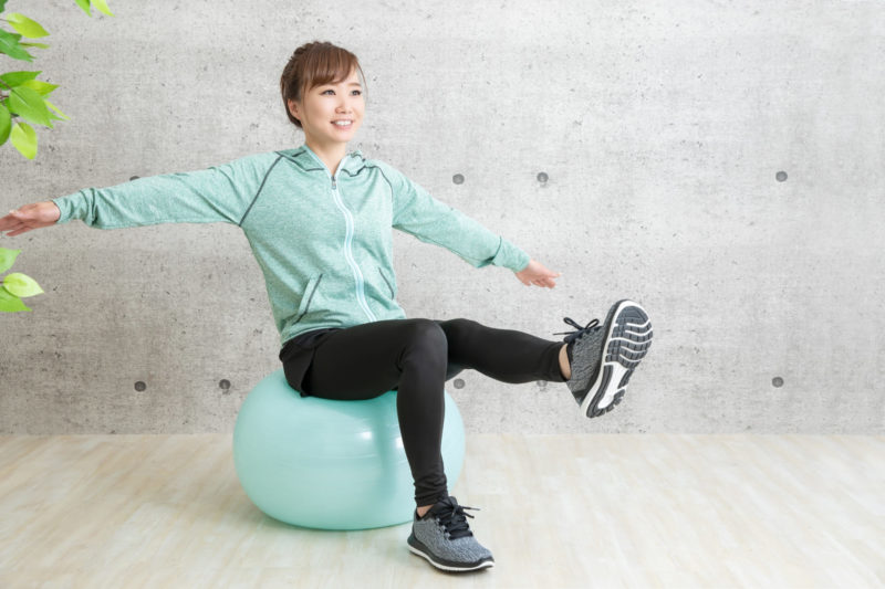 バランスボールの上で片足を上げてストレッチしている女性
