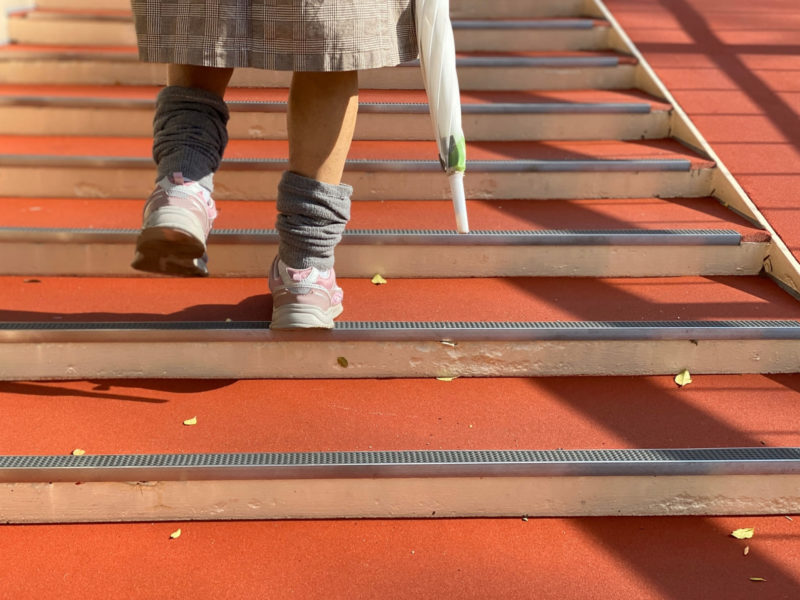 ゆるやかな赤い階段を上っている女性の足