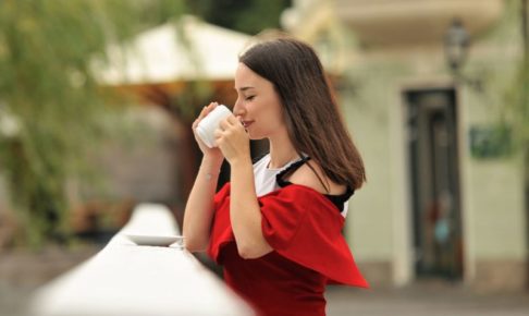 外で温かい飲み物を摂る赤い服の美女