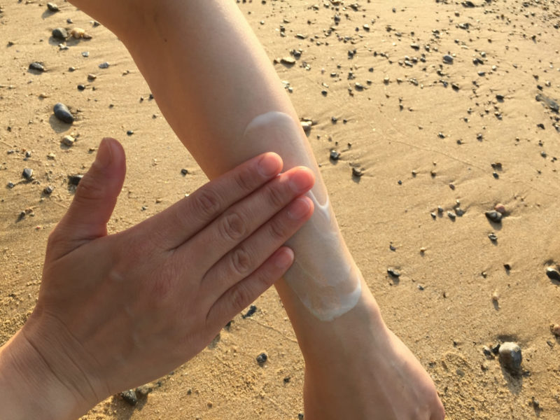 砂浜で左腕を念入りに日焼け止めを塗っているところ