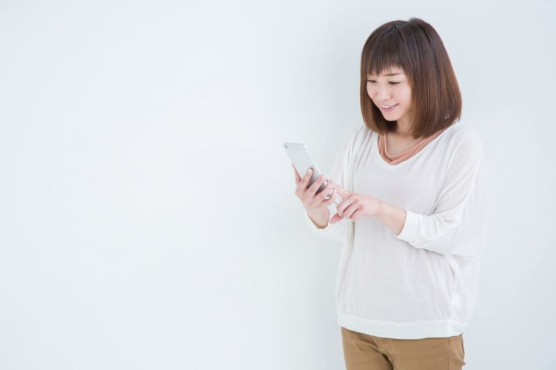 白い背景の中スマホを使おうとしている女性