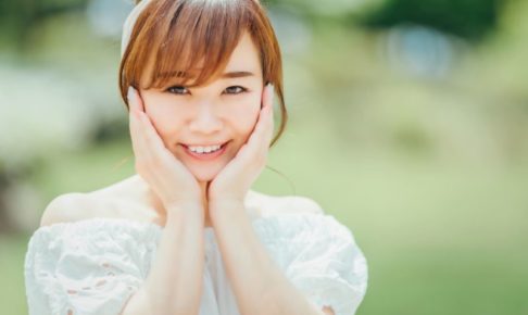 緑の外の中で顔に両手を当てて微笑んでいる女子