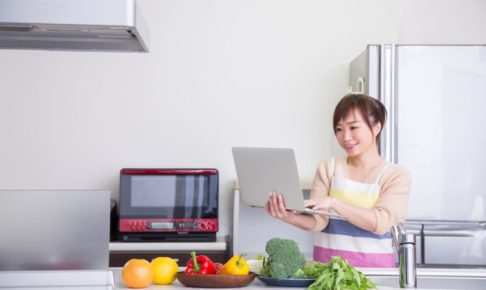 ノートパソコンでレシピを見ながら夕飯を作ろうとしている女性
