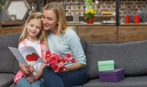 広そうなリビングのソファで小さな子供と絵本を読んでいる外国人ママ