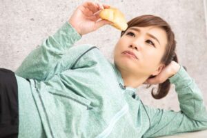 運動をサボって、寝ながら食べている女性