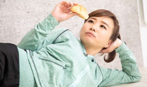 運動をサボって、寝ながら食べている女性