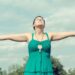 青空の下でワンピースの女性が手を広げているところ