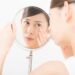 手鏡で目もとのたるみを気にする女性